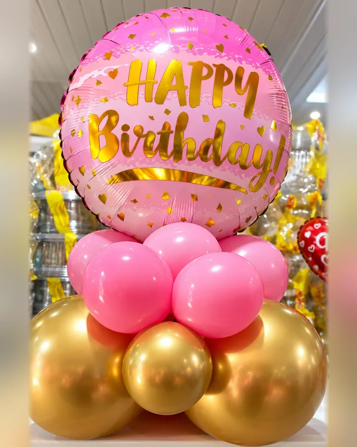 Balão rosa com a mensagem Happy Birthday em dourado e base de balões rosas e dourados.