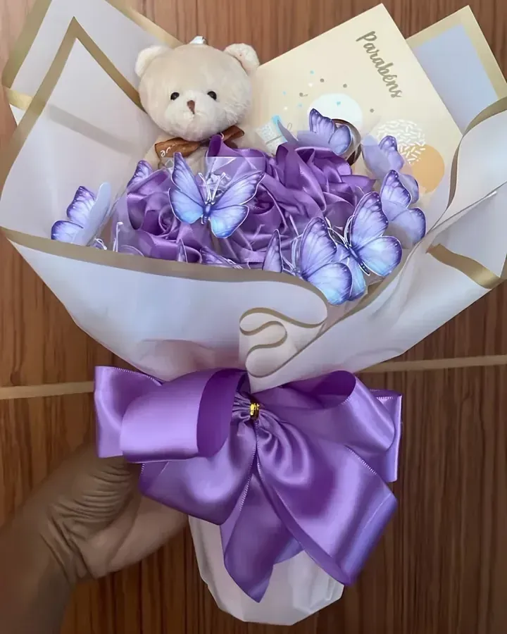 Rosas de cetim lilás com borboletas decorativas, ursinho e laço lilás. Feito por encomenda: consulte o prazo de produção e as opções de personalização.