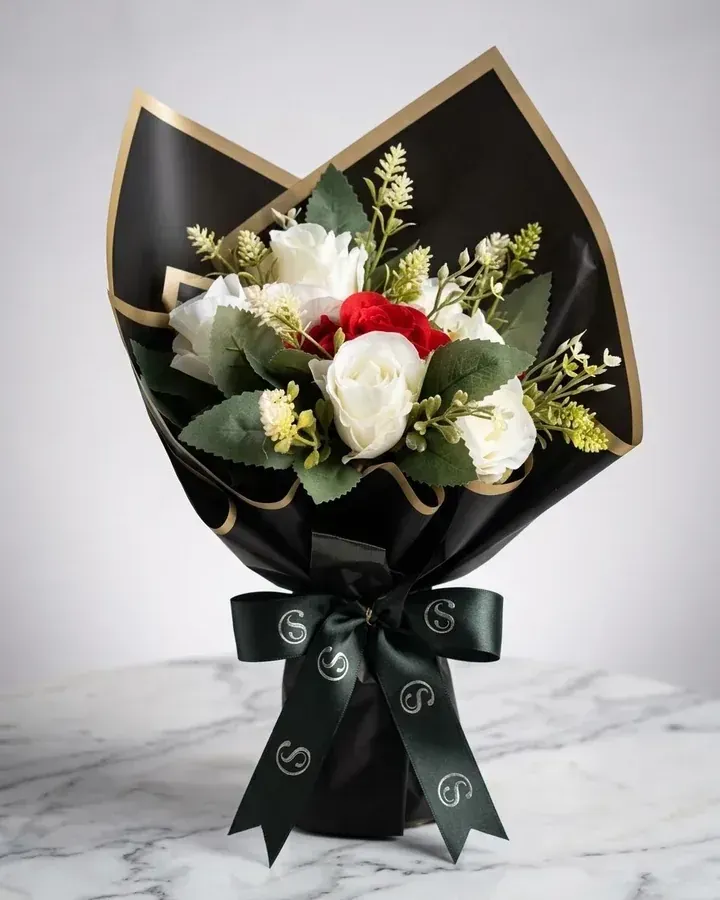 Rosas artificiais predominantemente brancas com detalhe vermelho e embalagem preta e dourada.