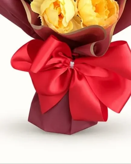 Rosas artificiais vermelhas e amarelas com embalagem marsala e laço vermelho.