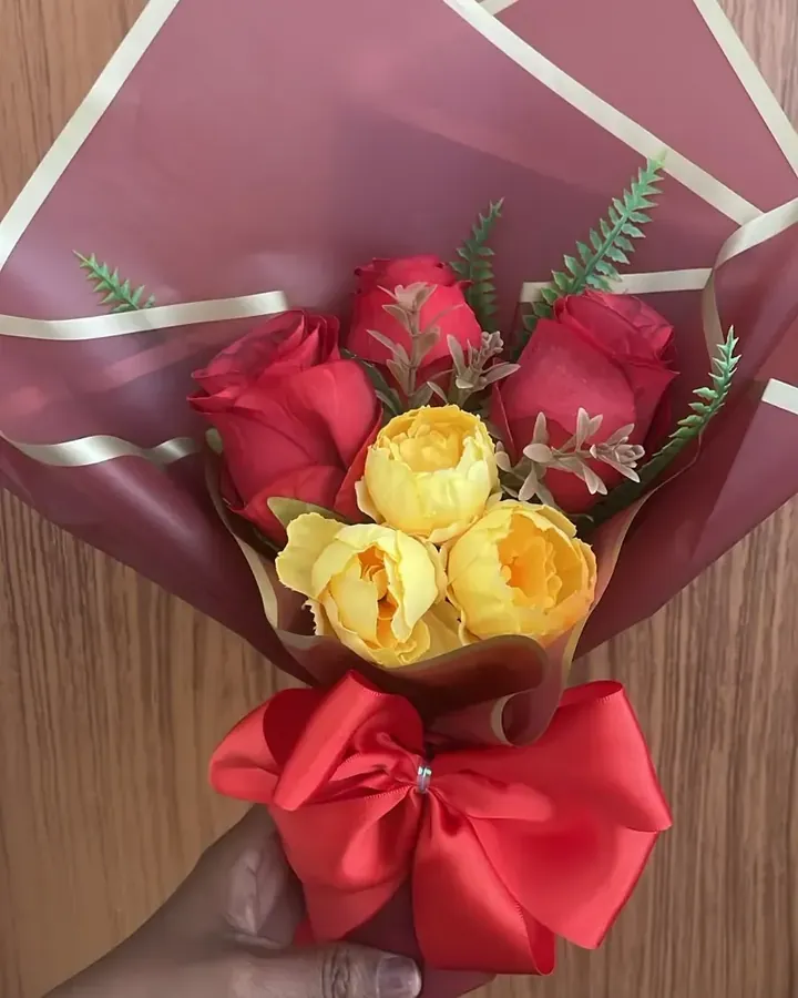 Buquê artificial completo de rosas vermelhas e peônias amarelas, com embalagem marsala e laço vermelho